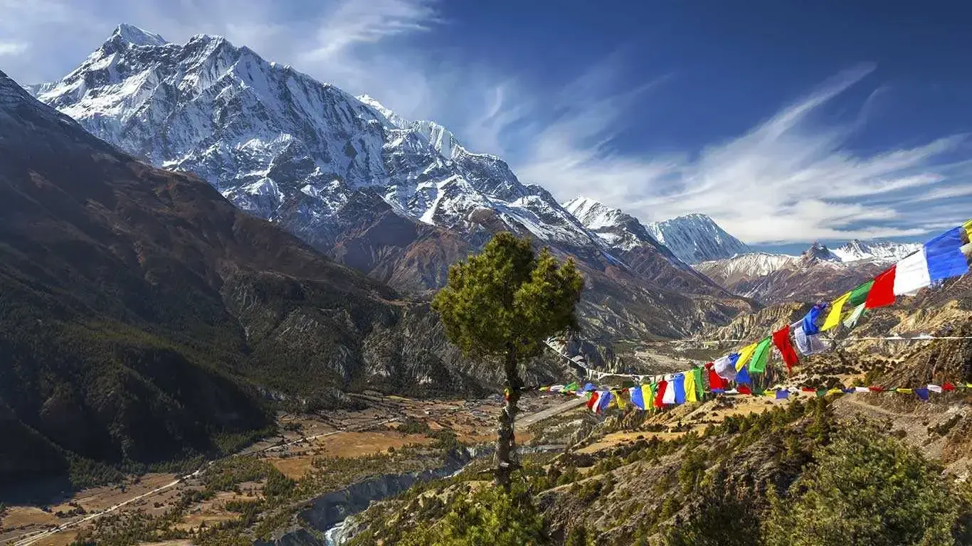 Snow-covered Himalayan peaks with prayer flags across the valley